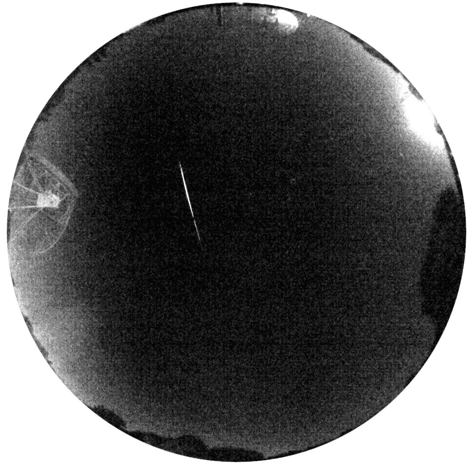 A circular all-sky view with the horizon around the outer edge. The Lovell Telescioe is visible at left, and in the middle is the streak of a bright fireball.